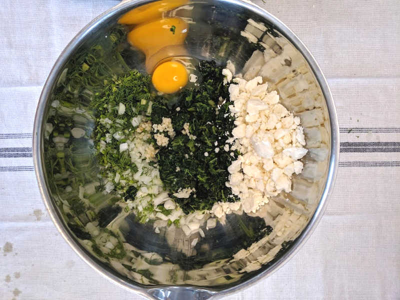 spinach, feta cheese, egg, onion and garlic in a silver mixing bowl