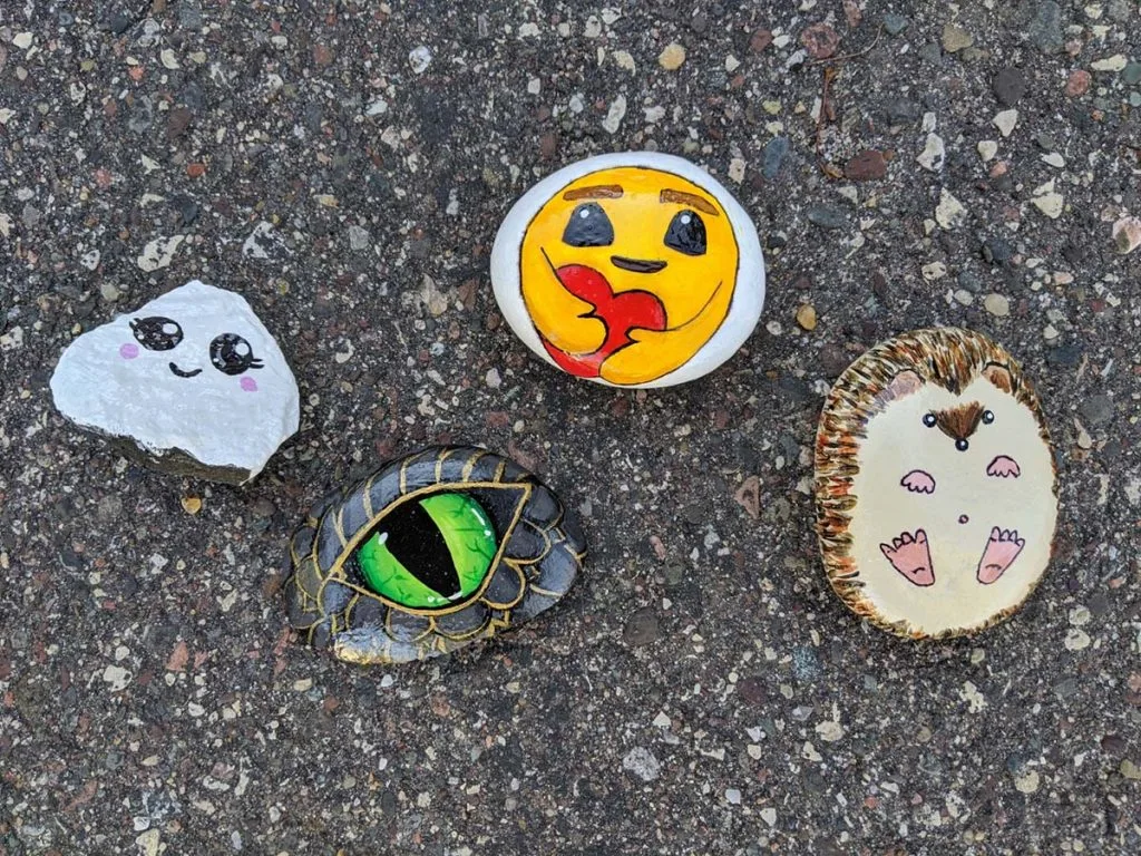 four painted rocks on a blacktop driveway.