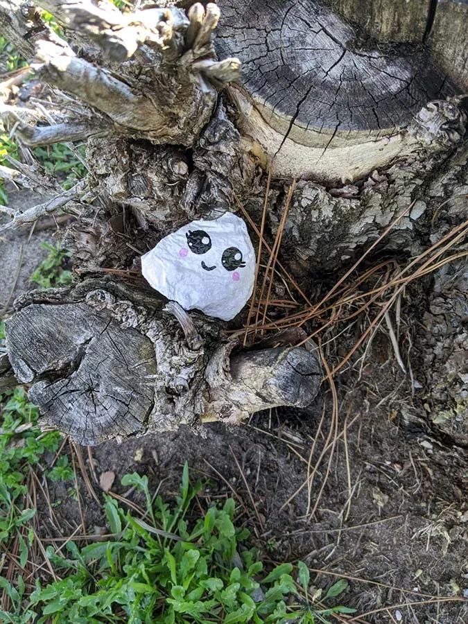 small painted rock with kawaii ghost face on a tree stump